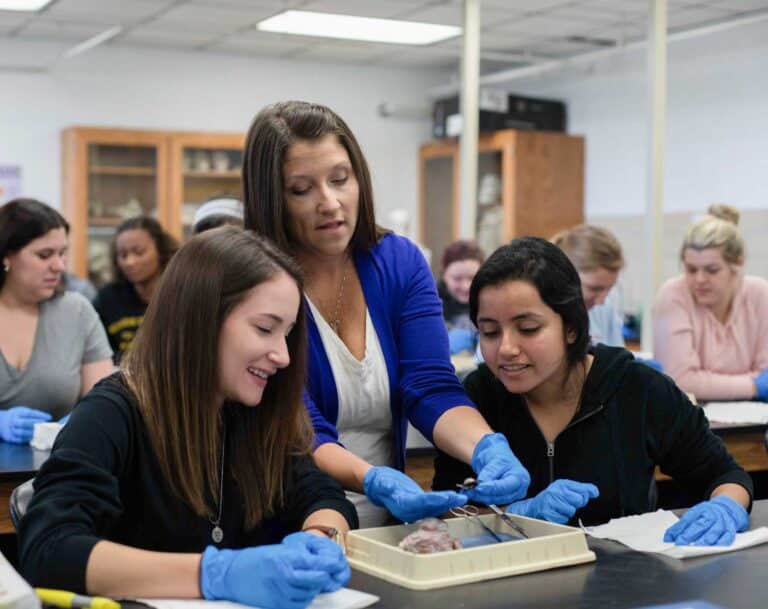 Teacher instructing students in a science lab on dissection techniques, all wearing gloves and focused on the task.